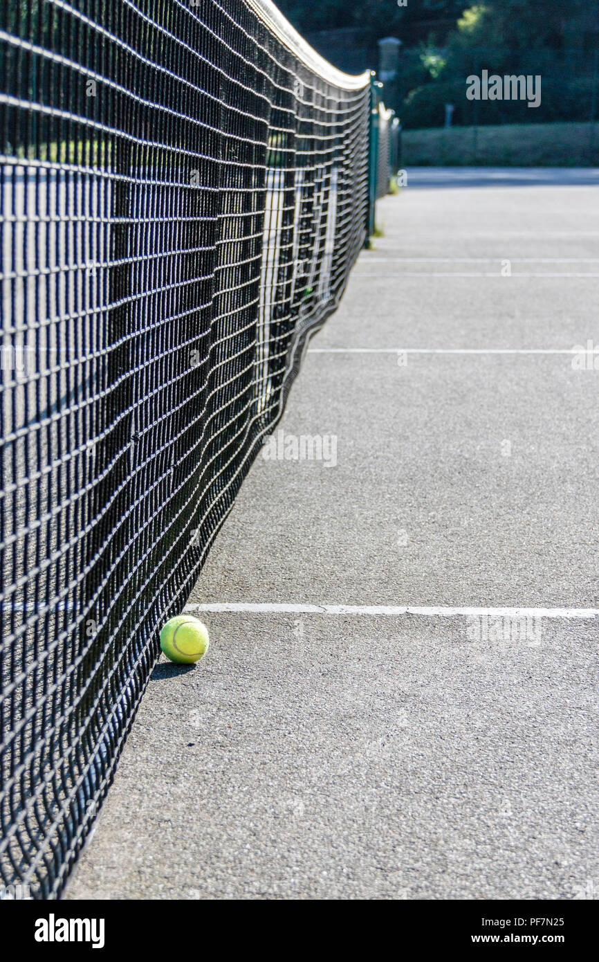 Low angle shot of of a yellow tennis ball on the ground next to the net of  a hard surface tennis court Stock Photo - Alamy
