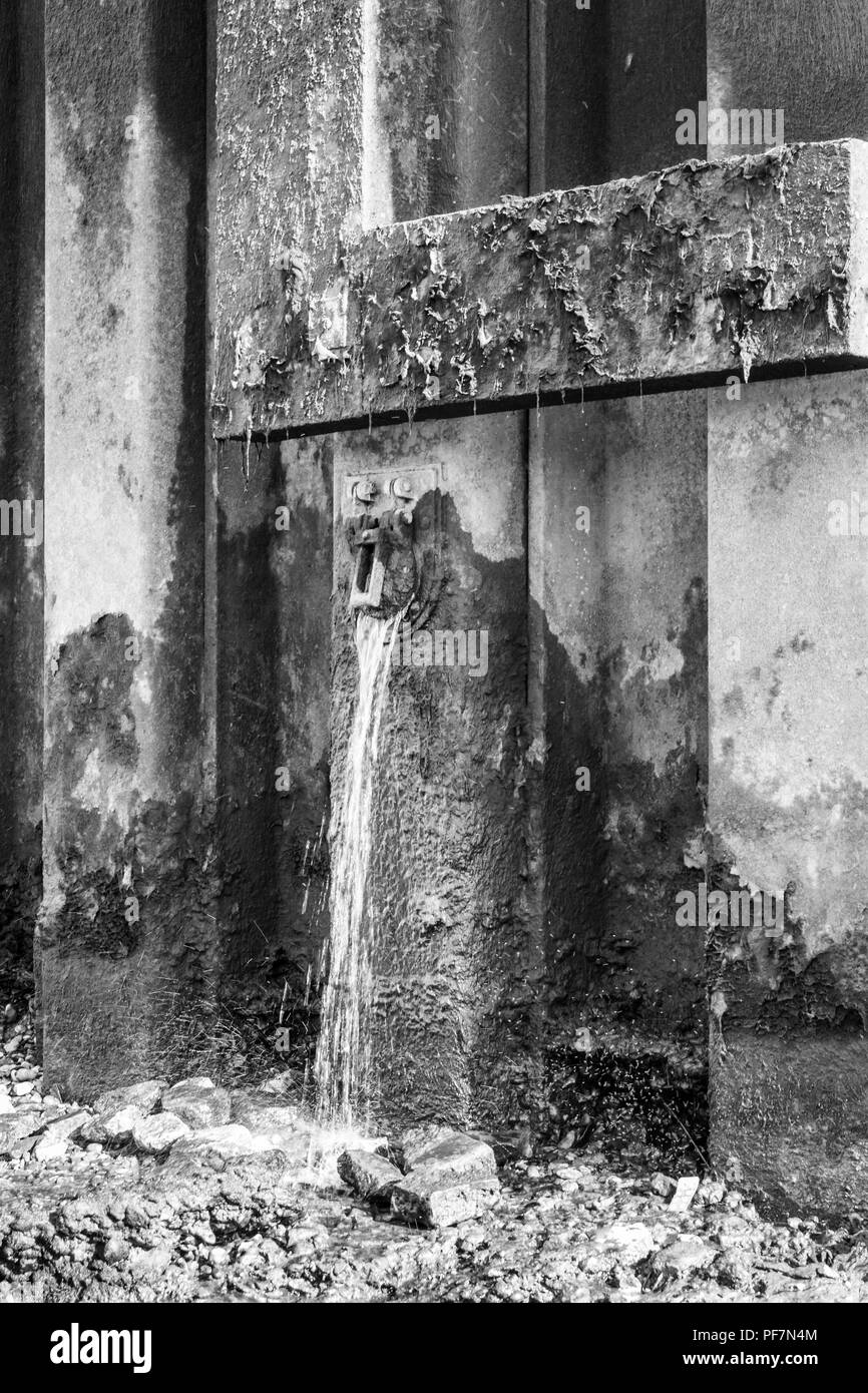Black and white image of metal reinforcement pilings on the south bank of the River Thames, water gushing from drainage outlets, Bankside, London, UK Stock Photo
