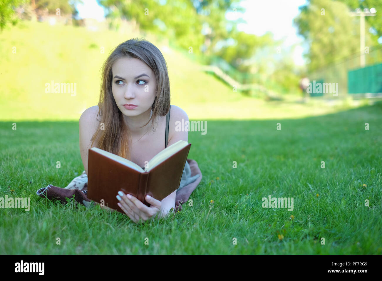 Young woman lies on green grass and reads book in the city park. Stock Photo
