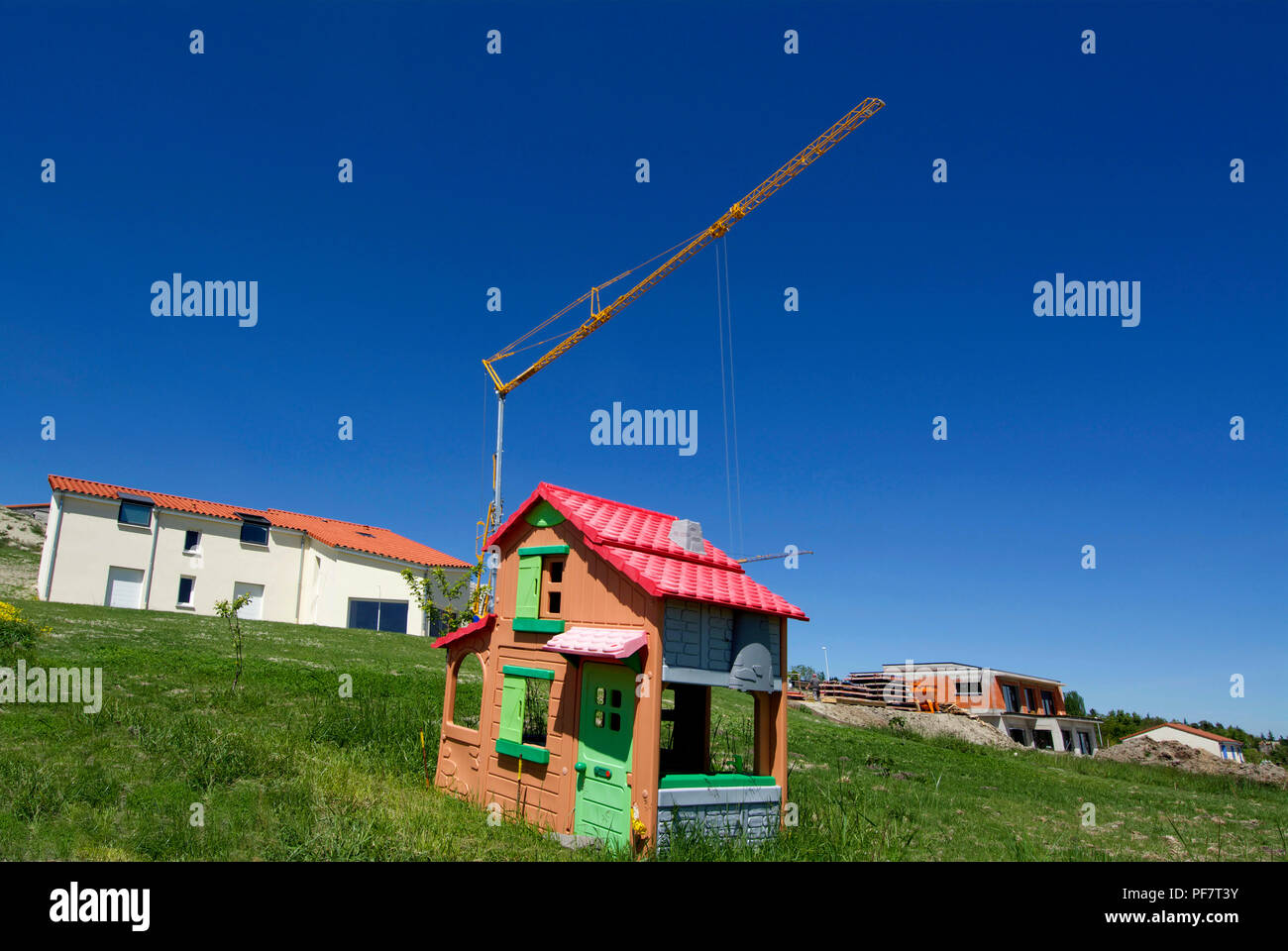 Plastic children's house on a ground with a crane and houses under construction, France Stock Photo