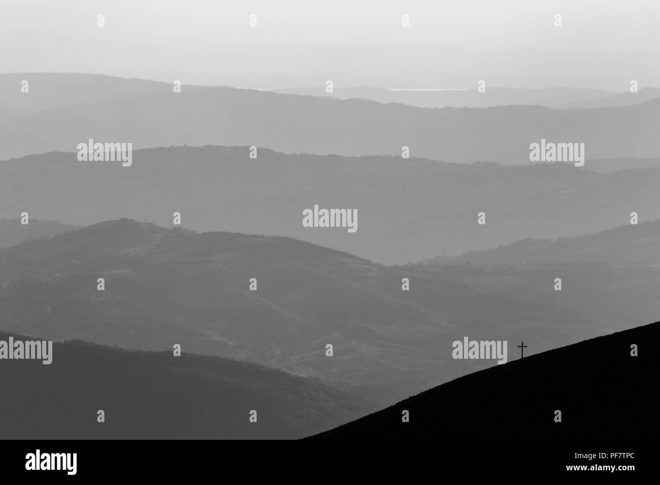 View of a cross on top of a mountain, with various others mountains layers in the background Stock Photo