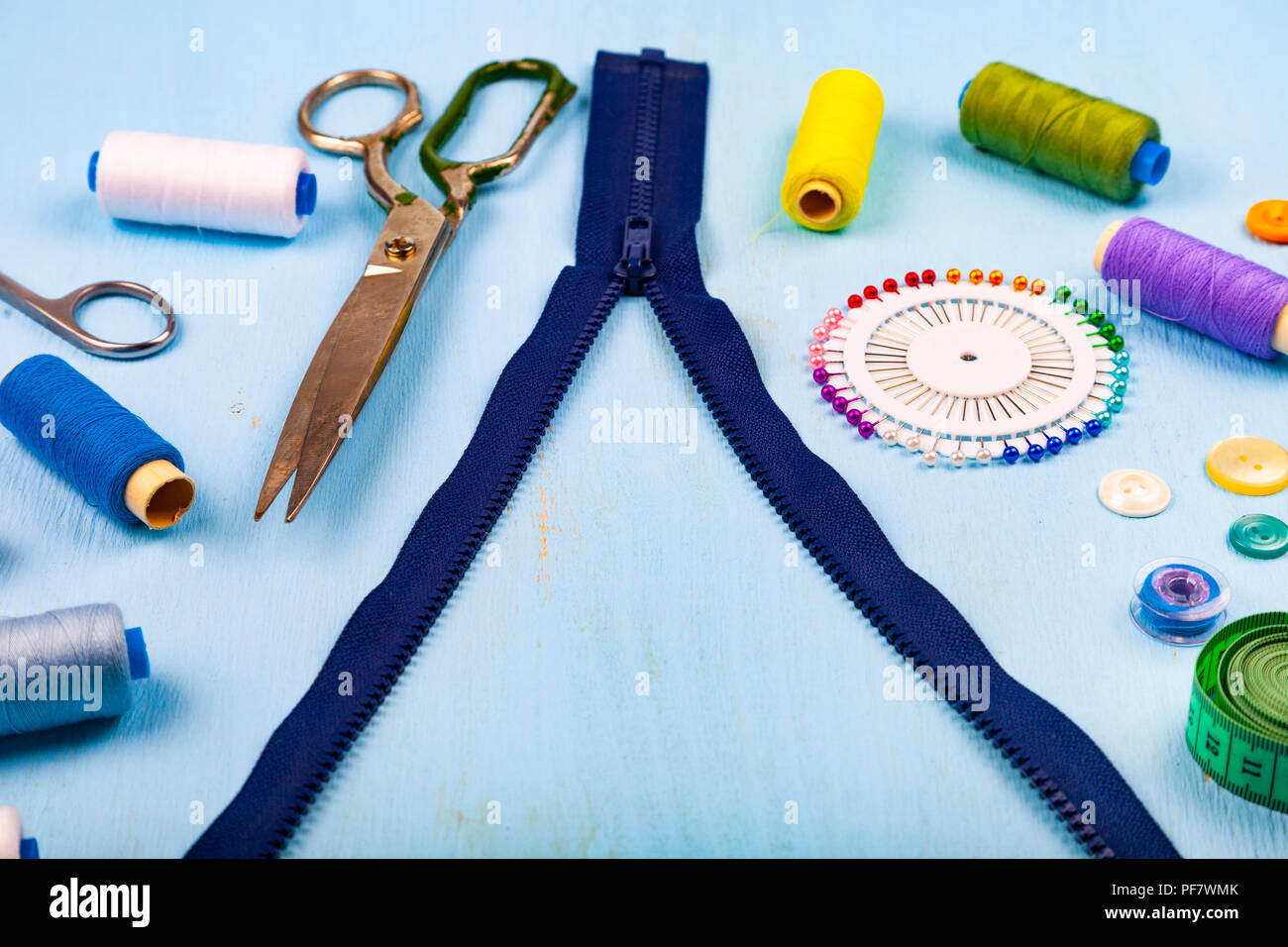 Unbuttoned zipper and sewing accessories on a blue wooden background ...