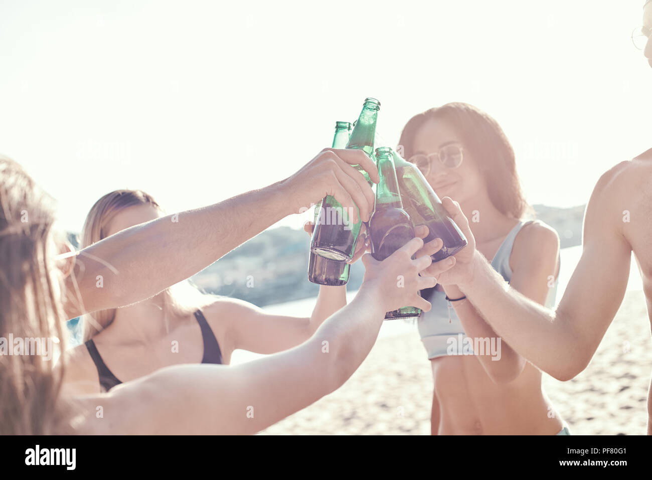 Enjoying carefree time with friends. Cheerful young people spending nice time together while sitting on the beach and drinking beer Stock Photo