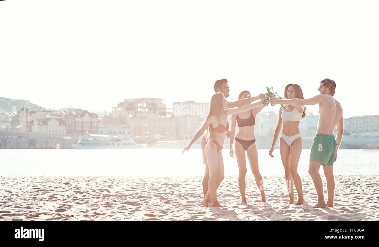 Enjoying carefree time with friends. Cheerful young people spending nice time together while sitting on the beach and drinking beer Stock Photo