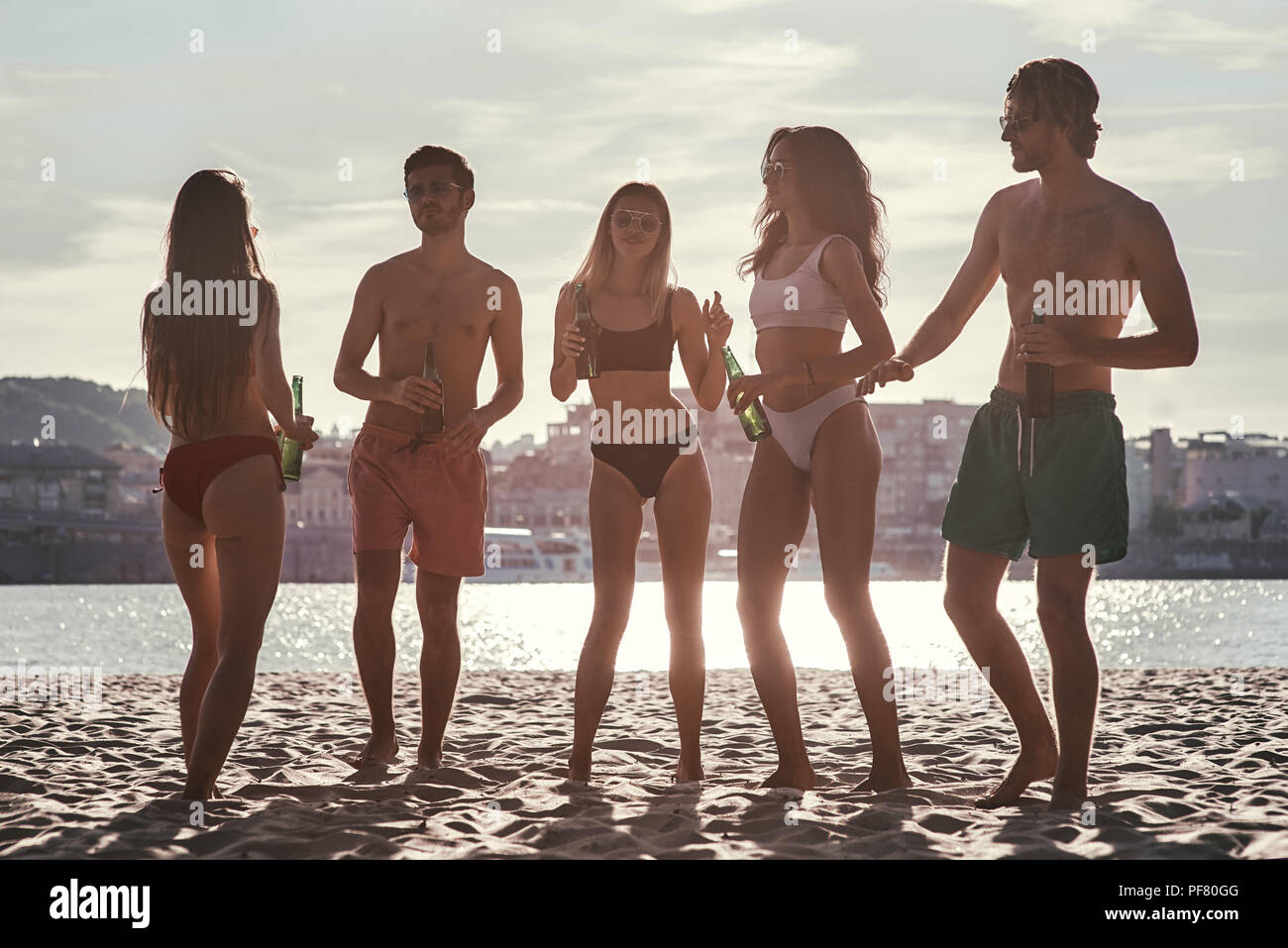 Enjoying carefree time with friends. Cheerful young people spending nice time together while sitting on the beach and drinking beer Stock Photo