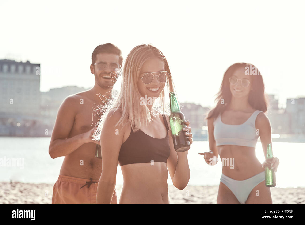 Enjoying carefree time with friends. Cheerful young people spending nice time together while sitting on the beach and drinking beer Stock Photo