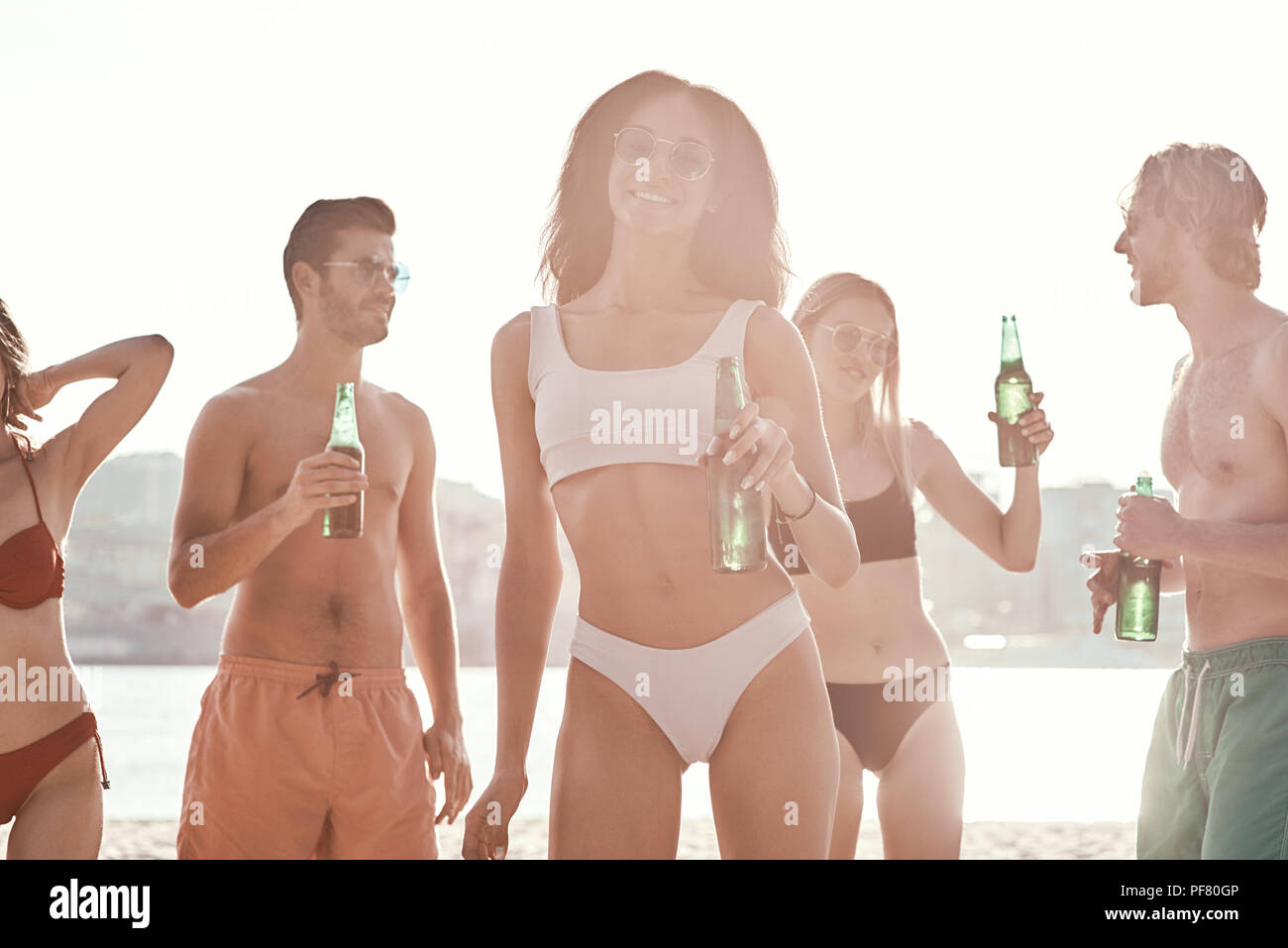 Enjoying carefree time with friends. Cheerful young people spending nice time together while sitting on the beach and drinking beer Stock Photo