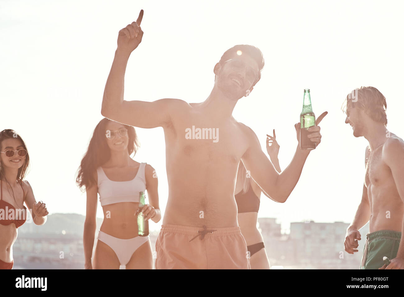 Enjoying carefree time with friends. Cheerful young people spending nice time together while sitting on the beach and drinking beer Stock Photo