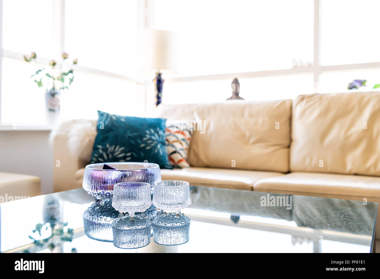 Interior of modern room with furniture, couch, sofa, pillows, glass table with reflection, bright natural light windows, lamp, flower vase and sunligh Stock Photo