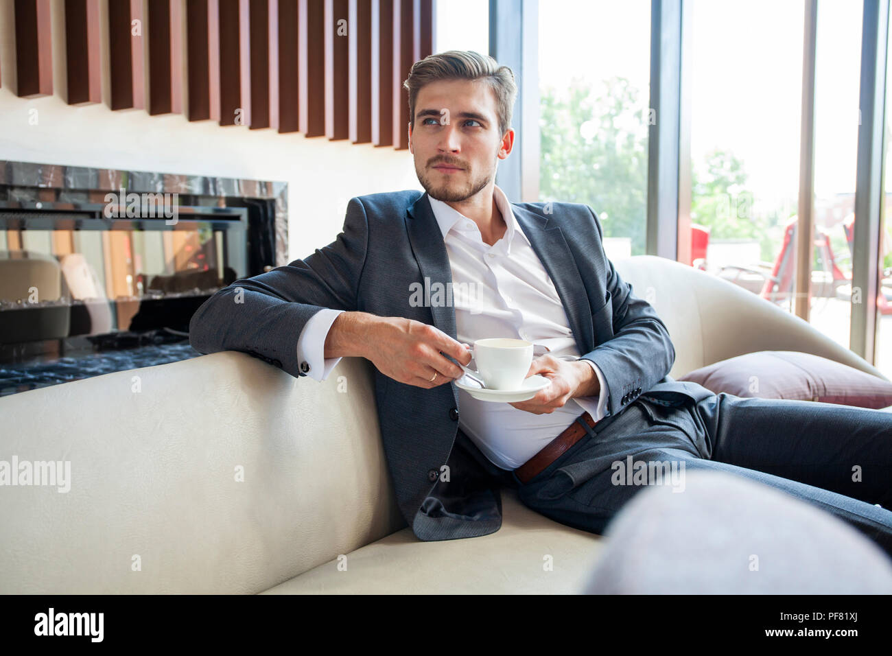 Portrait of happy young businessman sitting on sofa in hotel lobby. Stock Photo