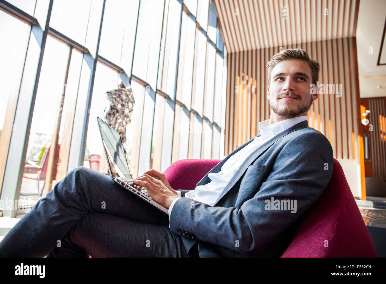 Young businessman working on laptop, sitting in hotel lobby waiting for someone. Stock Photo