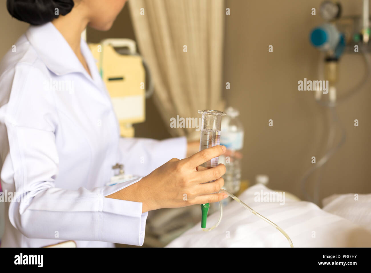 Nurse giving patient water using glass syringe to irrigate nasogastric