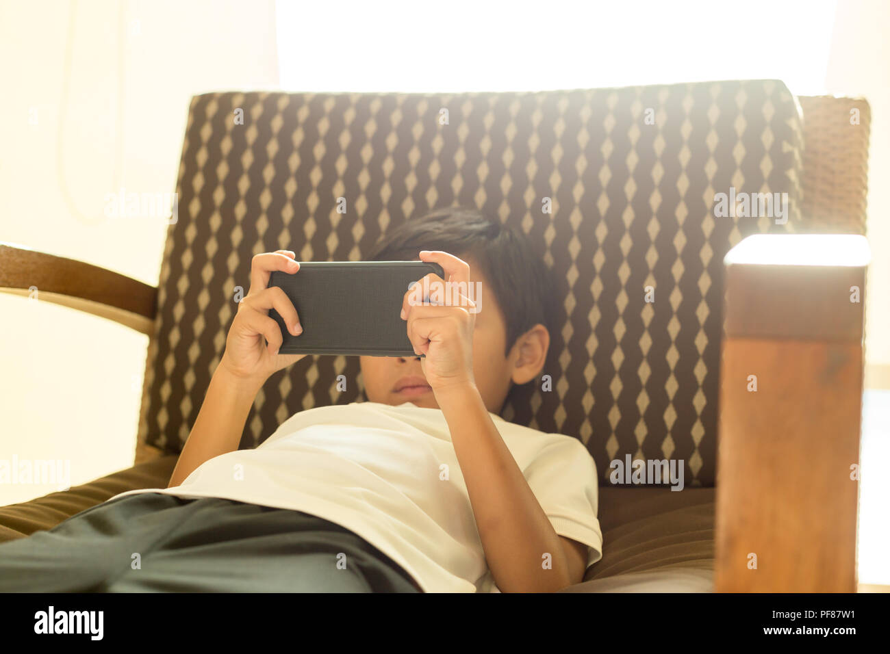 Asian Boy Using Cell Phone And Laying Down On Chair With Light