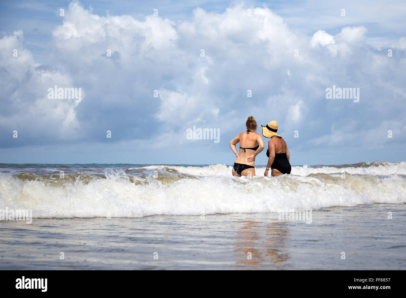 Mother and daughter in a swimsuit standing in a sea waiting for big