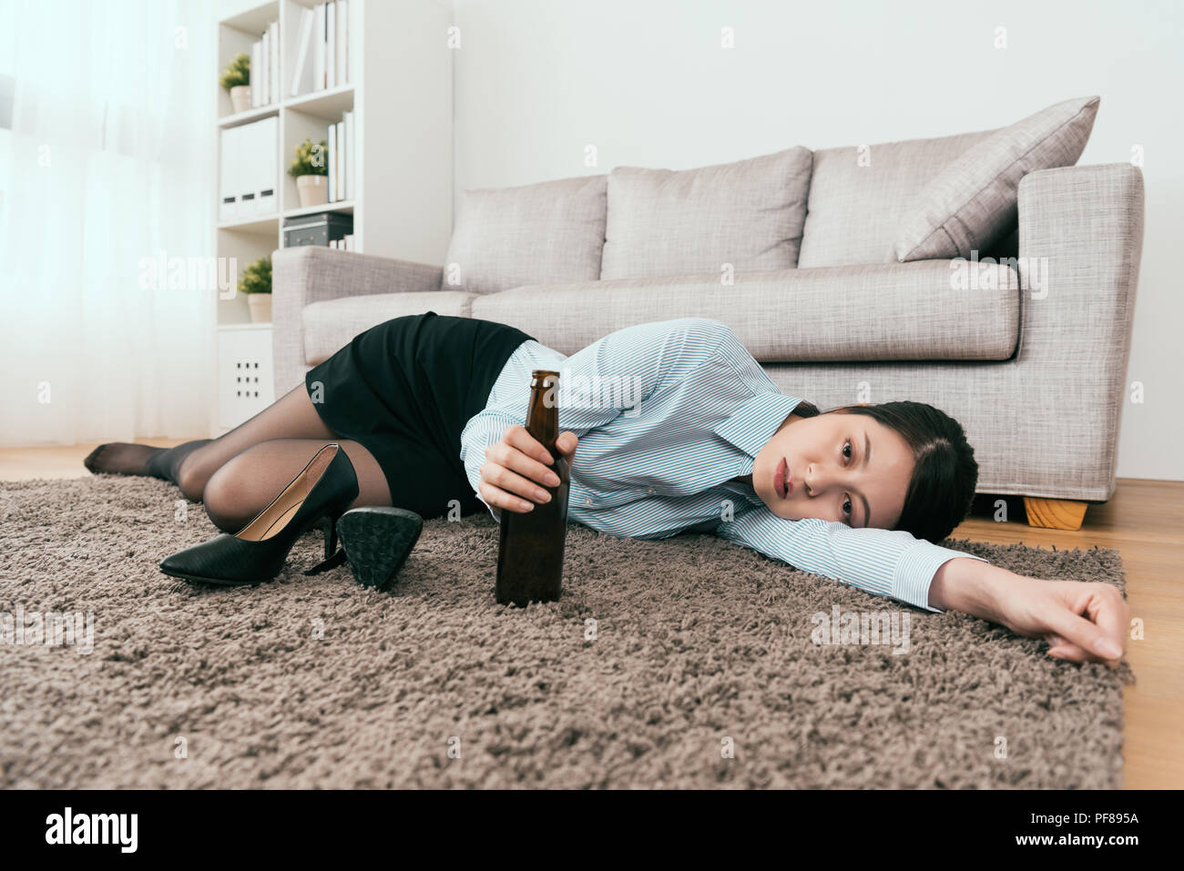 businesswoman manager is drunk from work and lie down on the floor of the living room and take off her high heel shoes at home Stock Photo