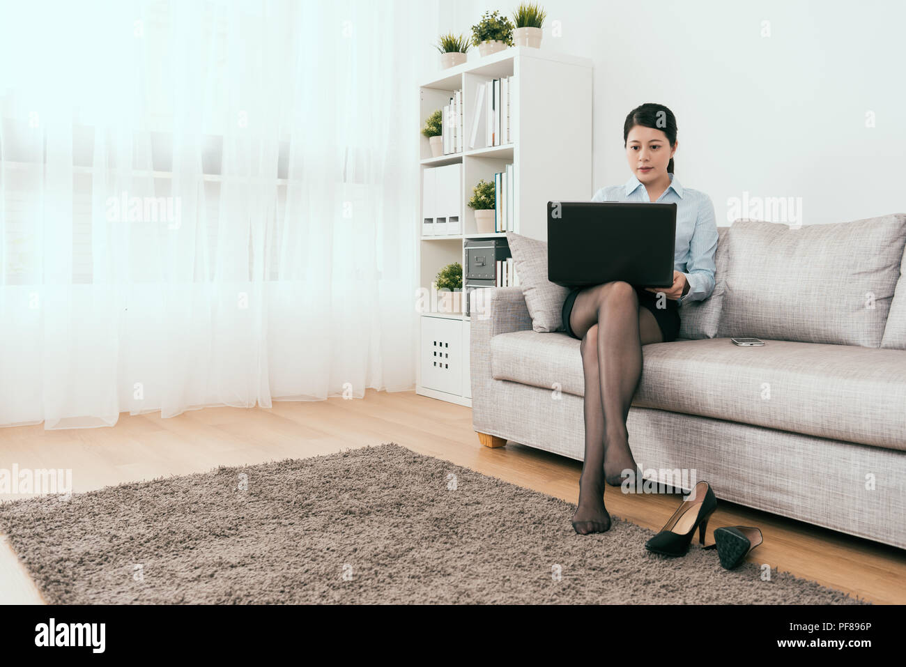 charming businesswoman using the notebook after work sitting on sofa at home Stock Photo