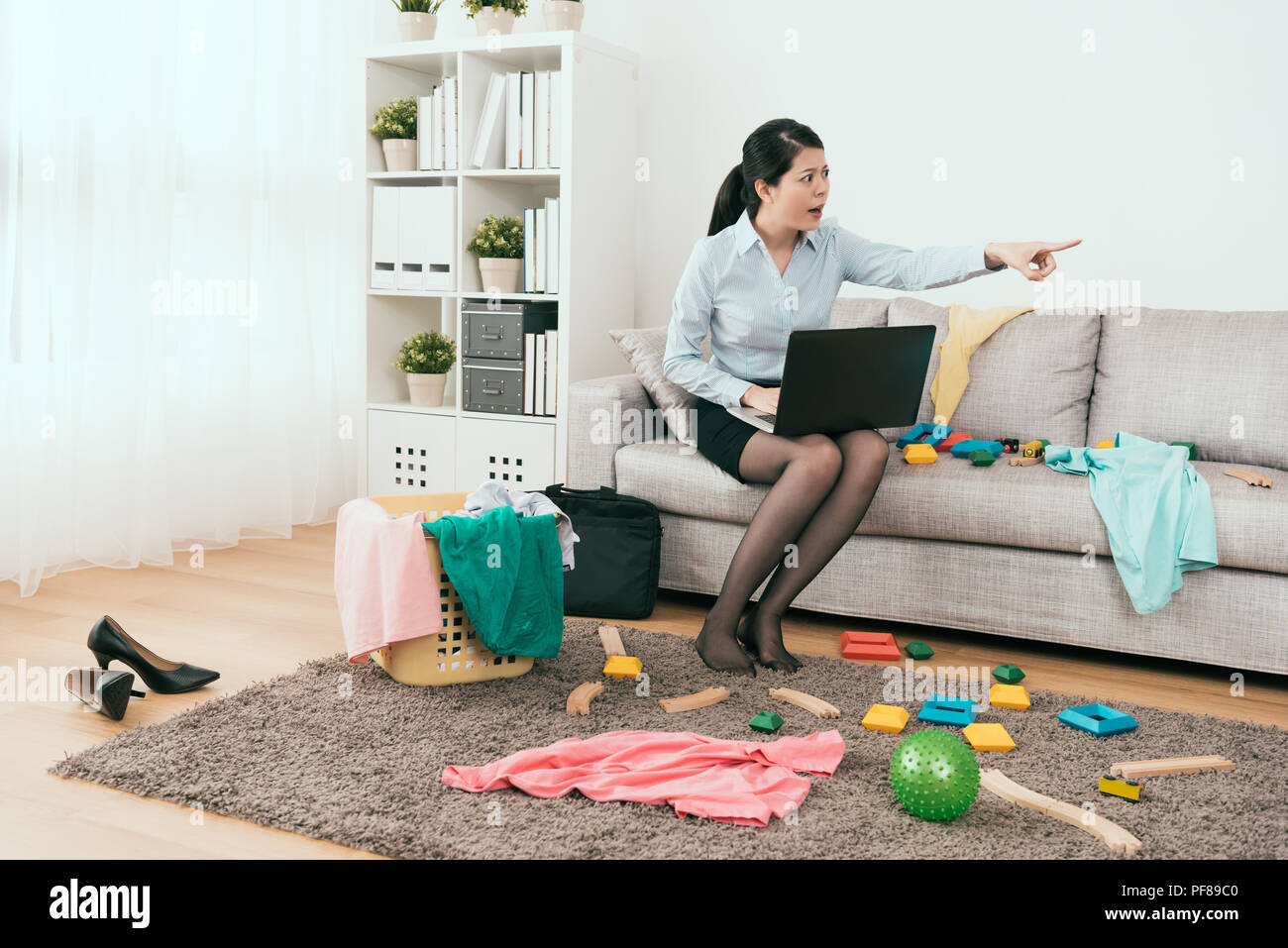 angry business housewife working at home and ask her kid to clean up the mess toys everywhere Stock Photo