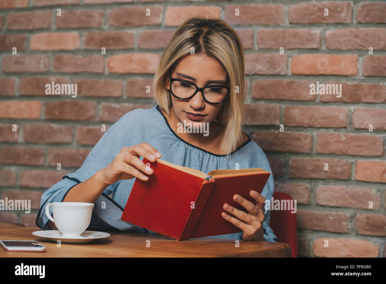 Woman sitting at a table reading a novel book. Stock Photo