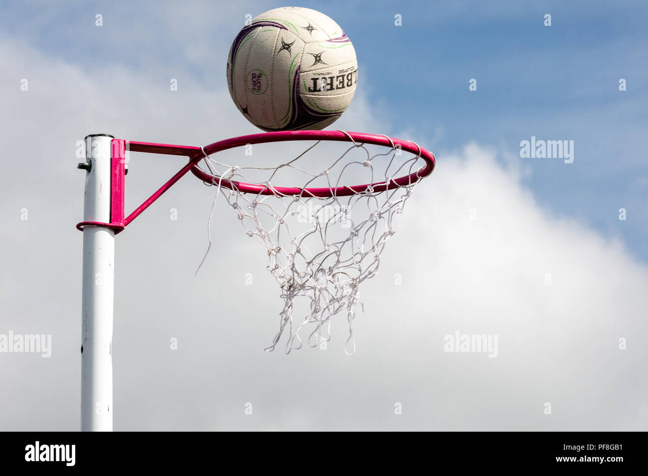 Netball posts with netball about to go through the net against a blue sky. Winning, Scoring Stock Photo