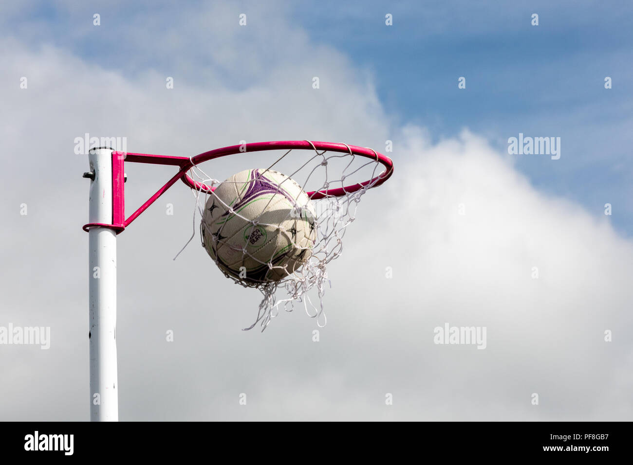Netball posts with netball going through the net scoring a goal against a blue sky. Stock Photo