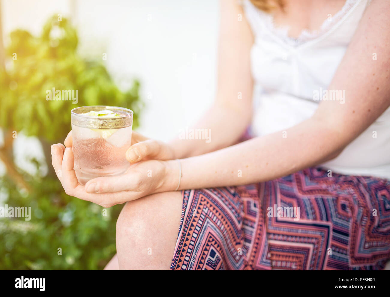 blond woman relaxing on patio holding iced drink Stock Photo