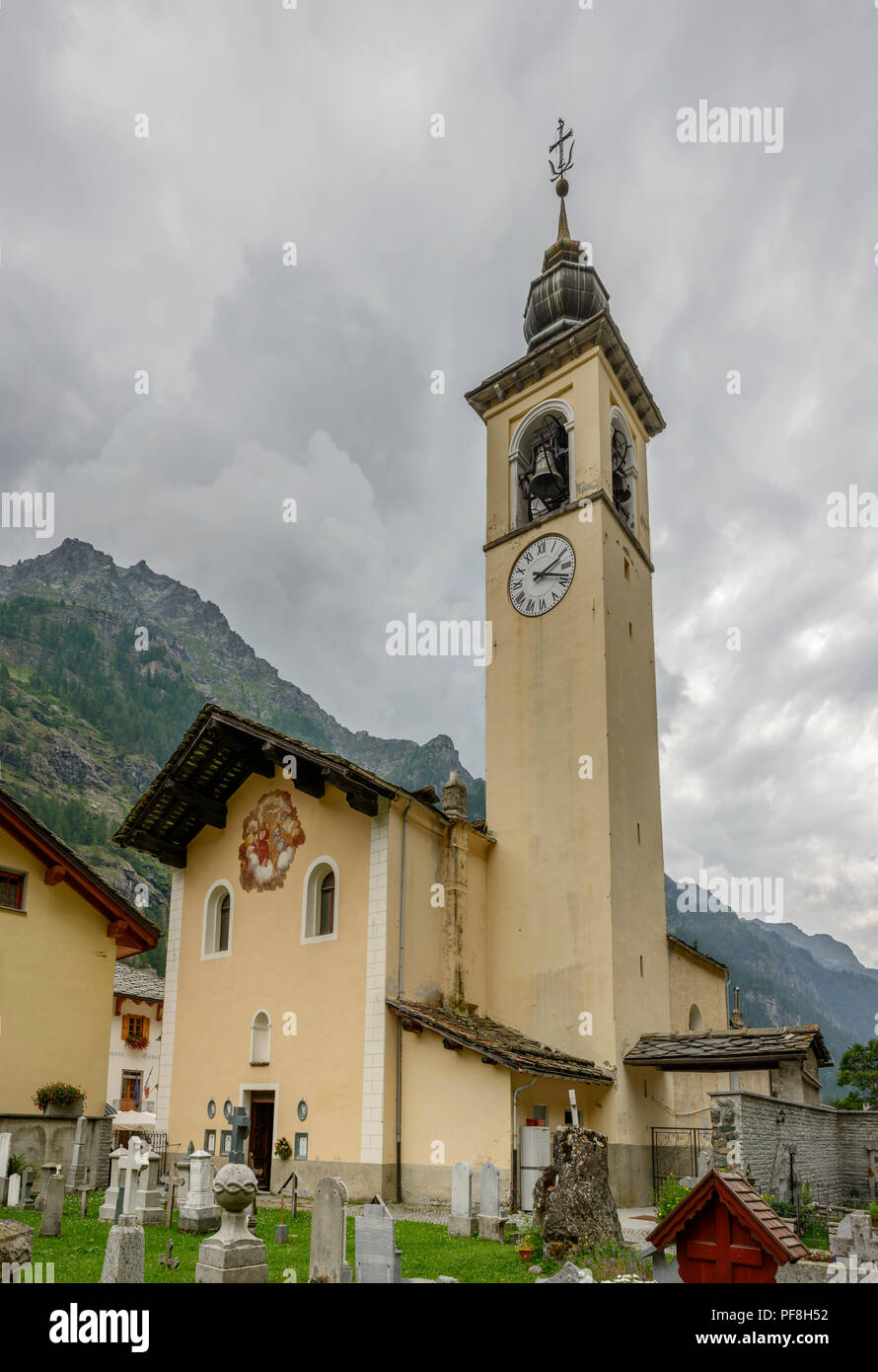 view of Holy Trinity church and belltower and of nearby graveyard, shot on a bright summer cloudy day at Gressoney la Trinite,  Lys valley, Aosta, Ita Stock Photo