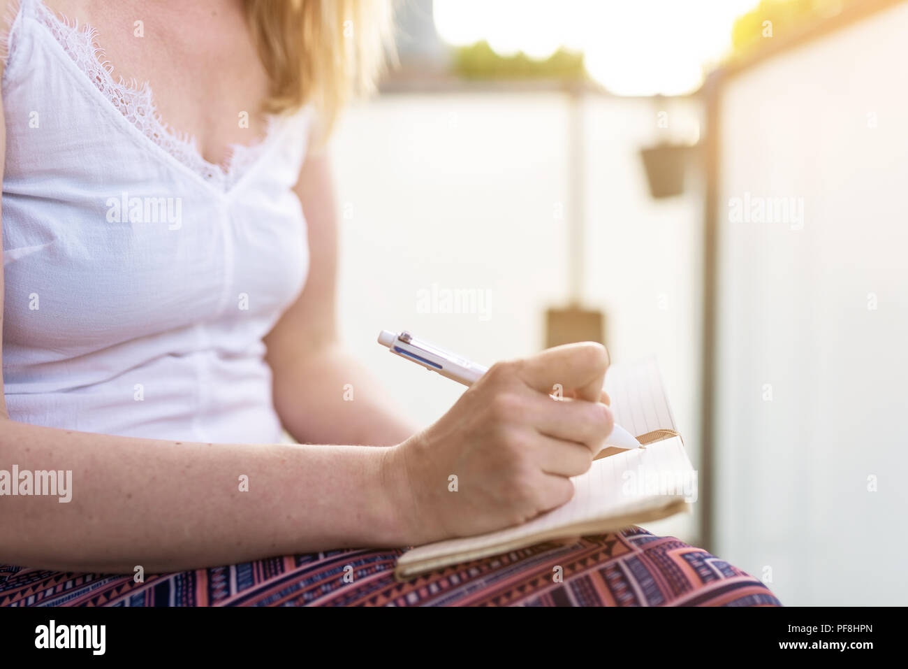 woman sitting on patio taking notes in notebook Stock Photo
