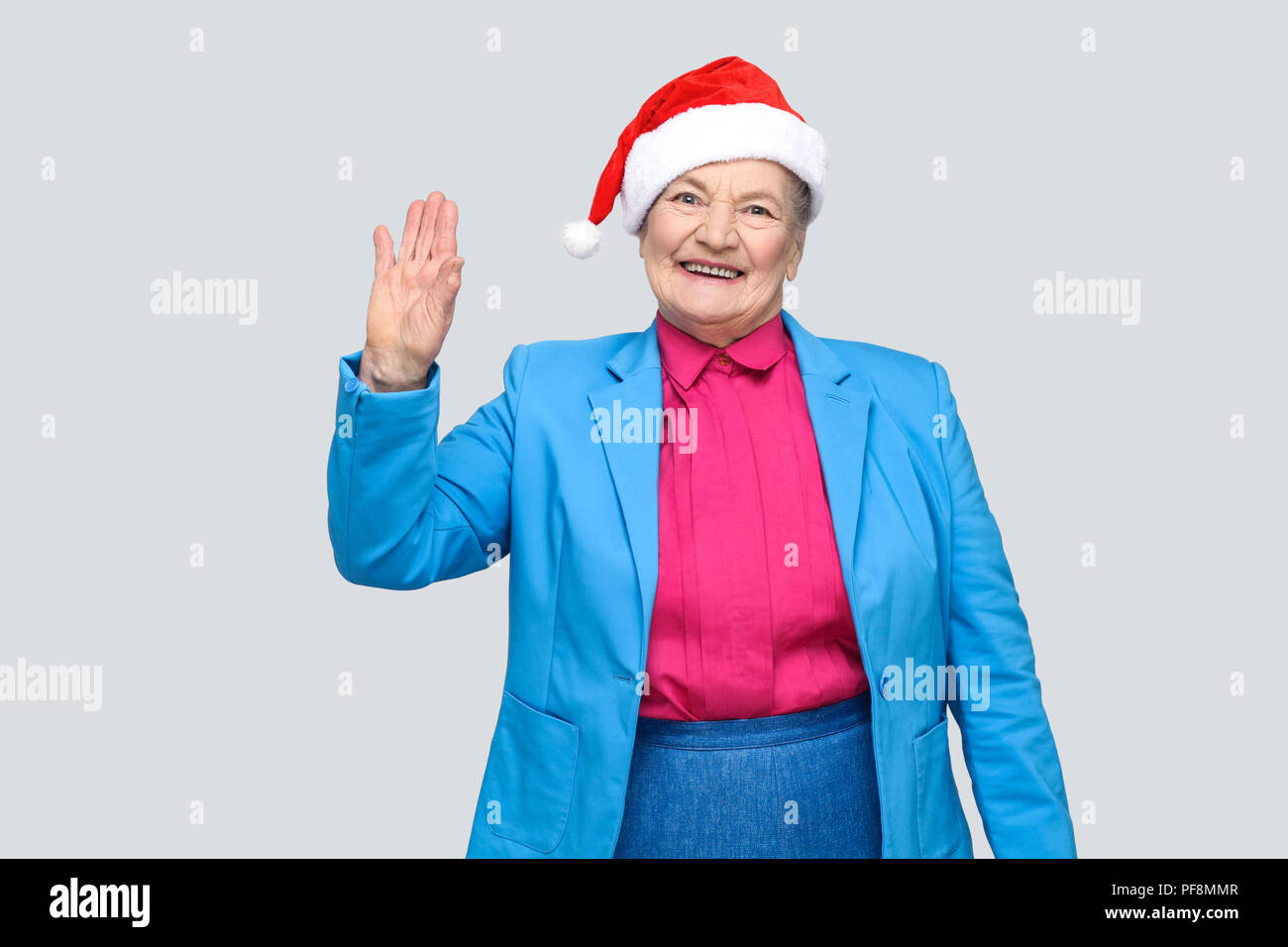Hi, nice to see you. happy toothy smiling colorful casual style aged woman with blue suit and christmas santa red cap standing and looking at camera.  Stock Photo