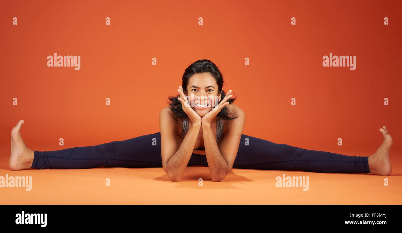 Wide Angle Seated Forward Bend yoga asana woman demonstrate on orange studio background Stock Photo