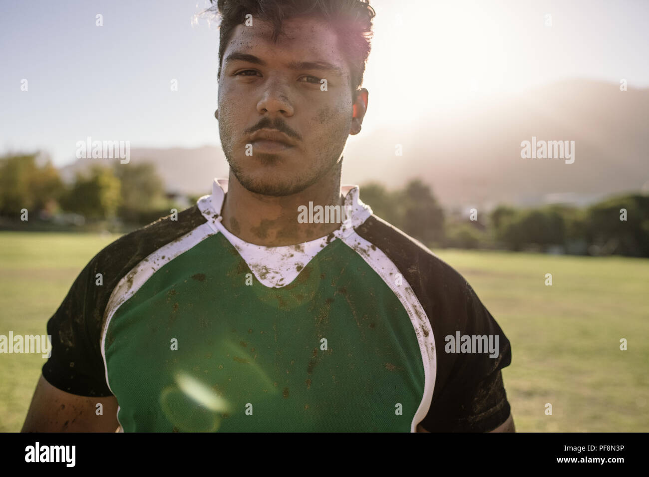 Rugby player on the sports field. Young sportsman with face and  uniform smeared in mud with bright sunlight. Stock Photo
