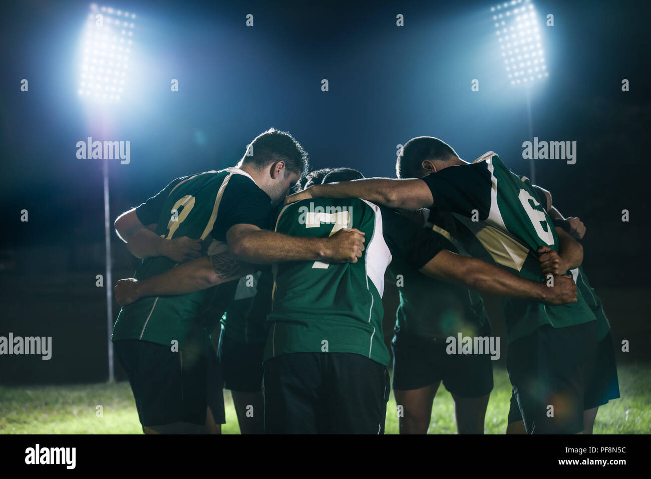 Rugby players standing together after the game under lights. Rugby team in huddle at sports arena at night. Stock Photo