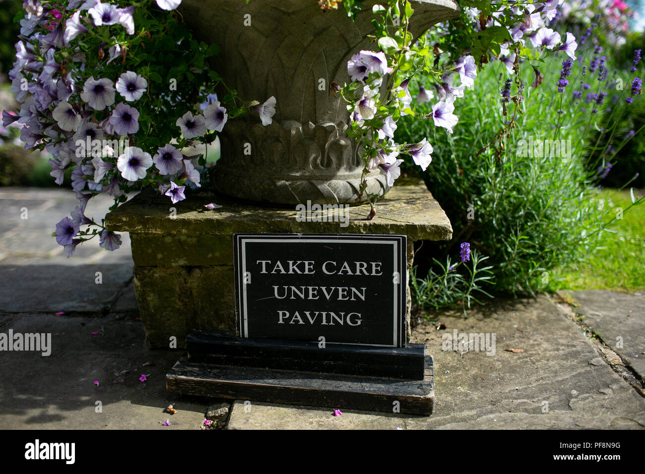 Closeup of take care uneven paving safety sign in an english country garden uk Stock Photo