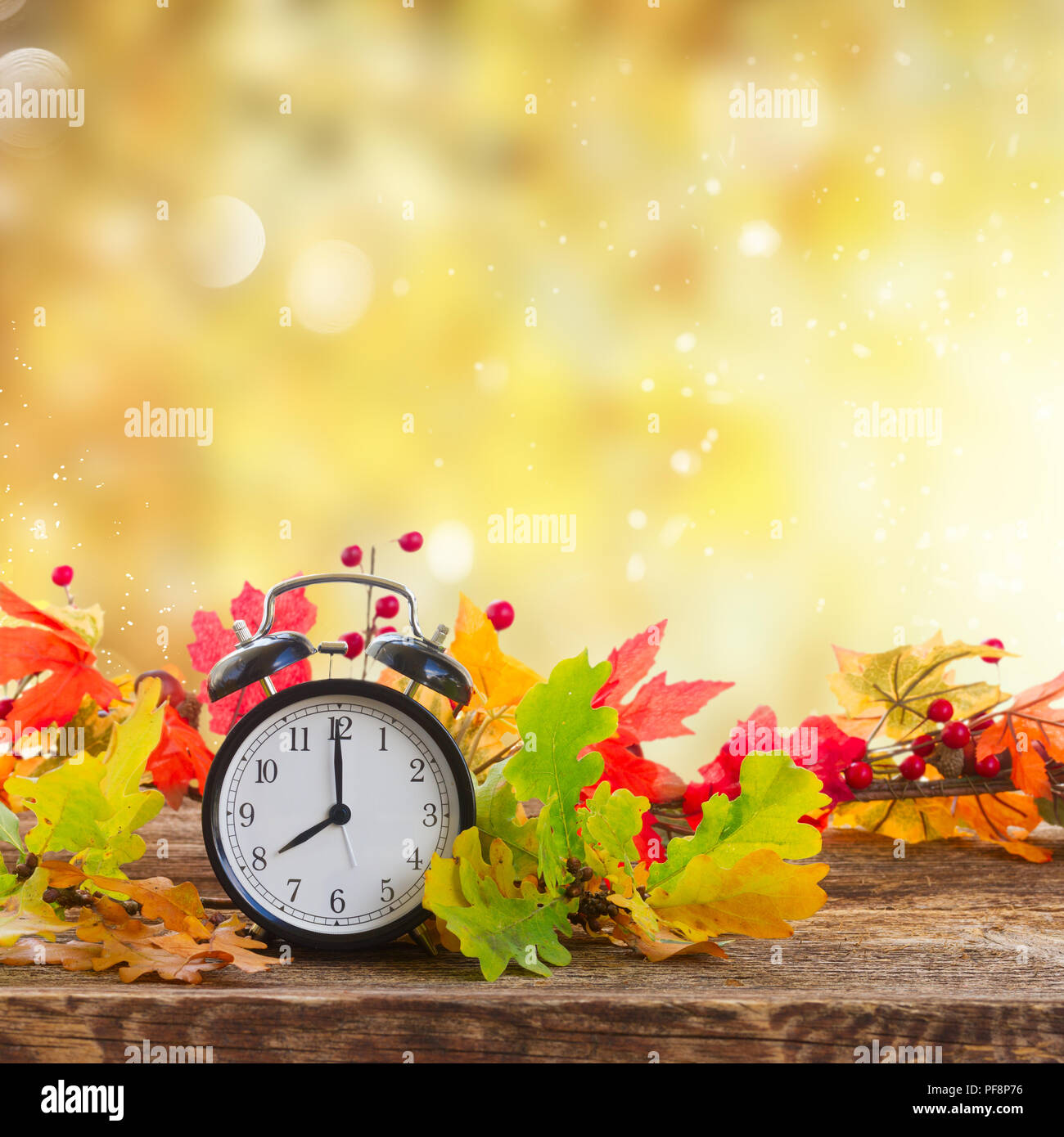 Autumn time - fall leaves with alarm clock over fall foliage background Stock Photo