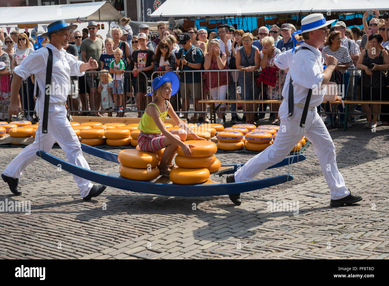 Alkmaar, Netherlands - July 20, 2018: Traditional cheese carriers carrying a little girl sitting on their cheese stretcher Stock Photo