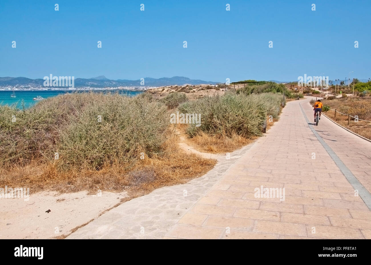PALMA DE MALLORCA, SPAIN - JULY 21, 2012: Bicyclist in orange cycling along the track through coastal dry herb landscape on July 21, 2012 in Mallorca, Stock Photo