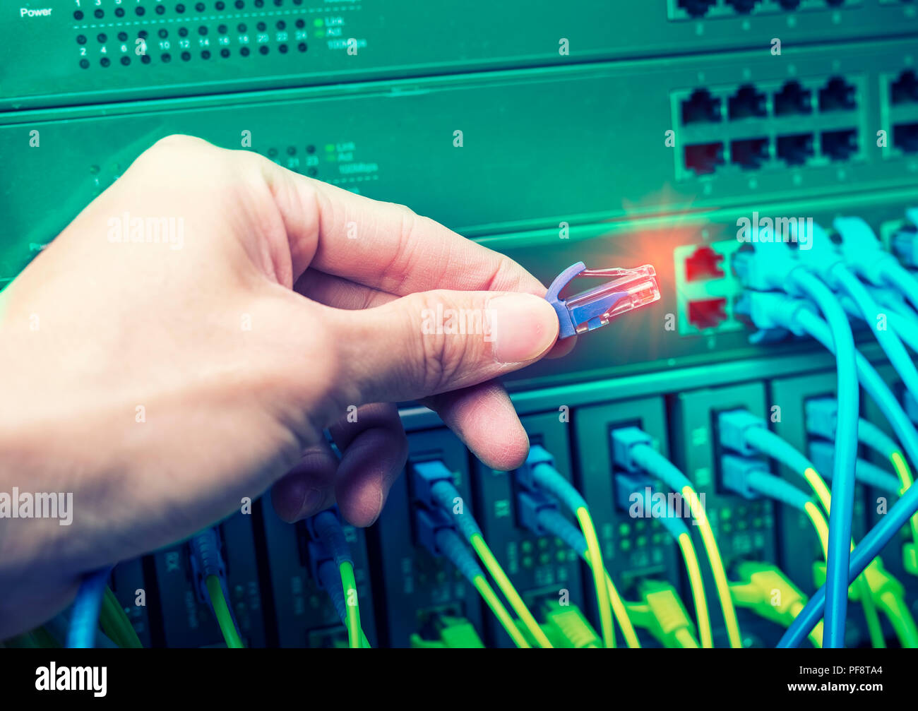 administrator holding network cables connected to servers Stock Photo