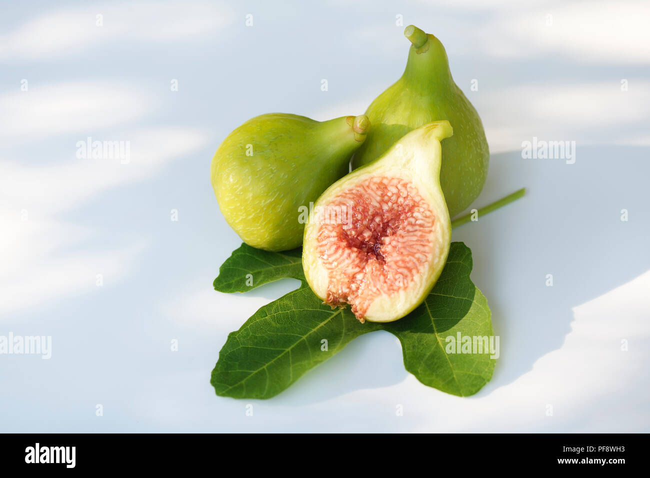 Freshly picked, ripe, organic Kadota figs on a fig leaf, with one fruit sliced in half showing red pulp, artistic food still life isolated on white ba Stock Photo