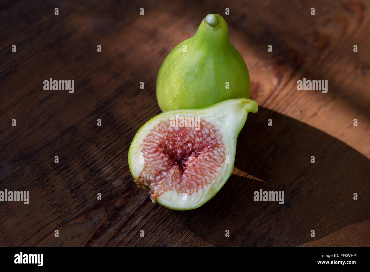 Organic, freshly picked ripe Kadota figs on a table, one fruit sliced in half showing purple pulp, artistic food still life on wood background Stock Photo