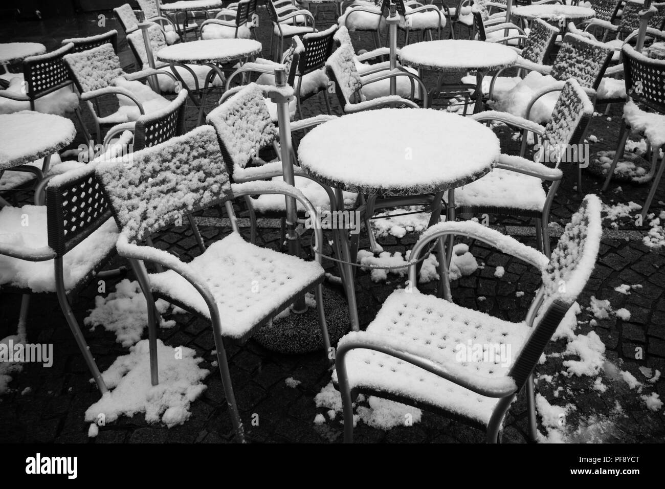 street restaurant chairs and tables stand empty covered with fresh snow on a street in German town Fussen, April 2017 Stock Photo