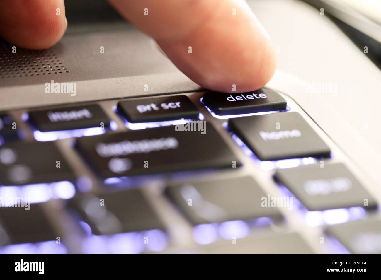 close up of a finger hitting pushing the delete symbol button tab on an illuminated laptop computer key board. The delete key Stock Photo