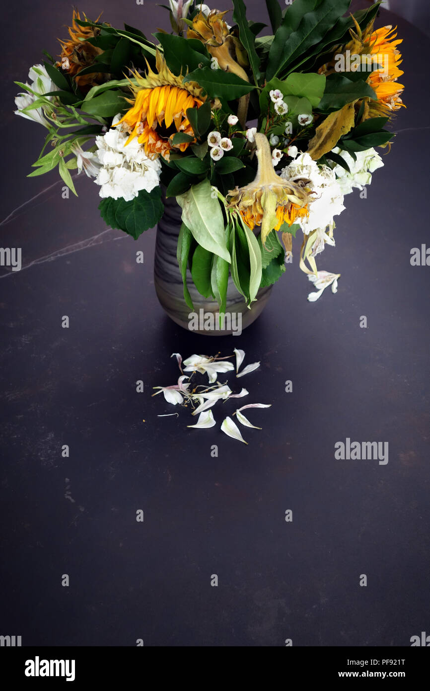 Looking slightly down at a vase of dying flower arrangement, large once bright now dying sun