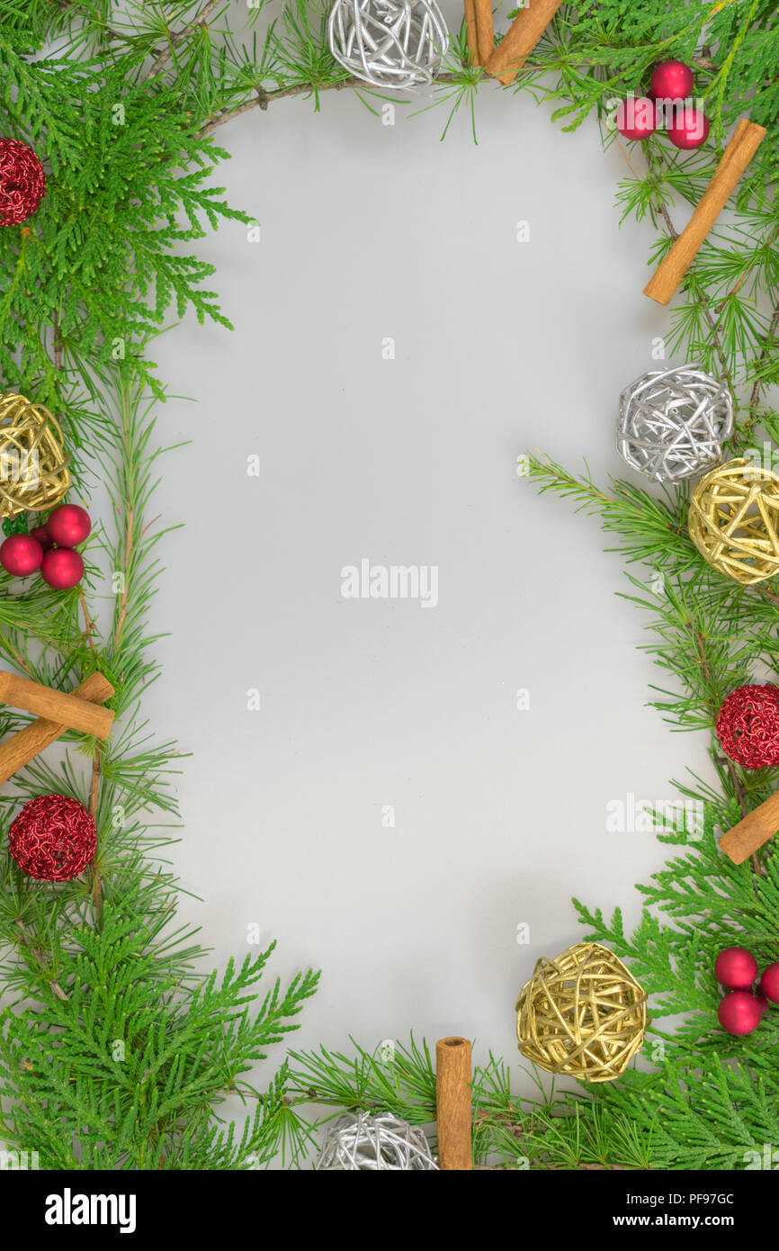 a border of cedar, white pine, and tamarack branches with  cinnamon sticks, twine and twig balls, berry clusters, and red ornaments with copy space in Stock Photo
