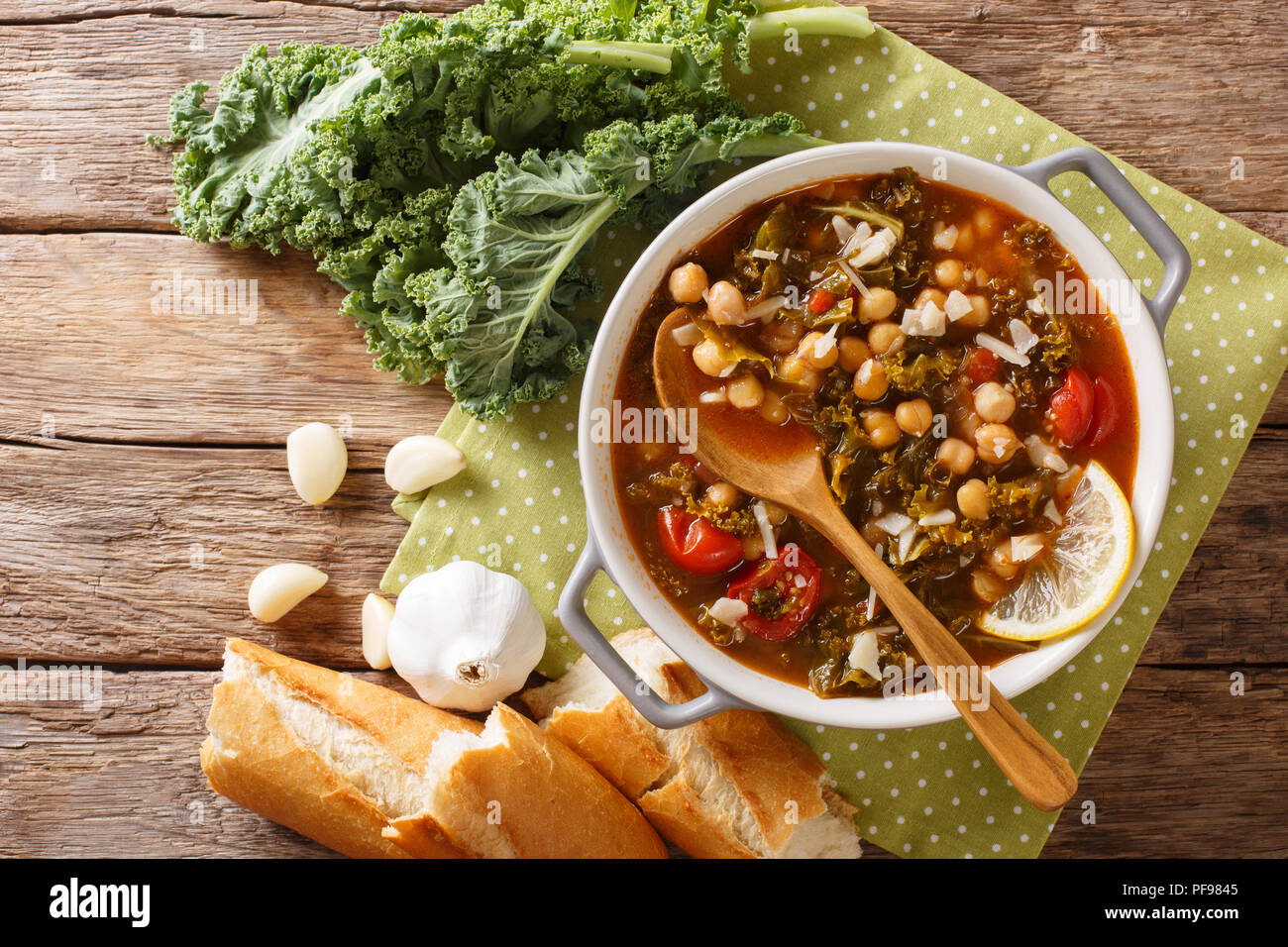 Soup of chickpeas, kale, tomatoes, garlic and potatoes with lemon close up in a bowl on the table. horizontal top view from above Stock Photo