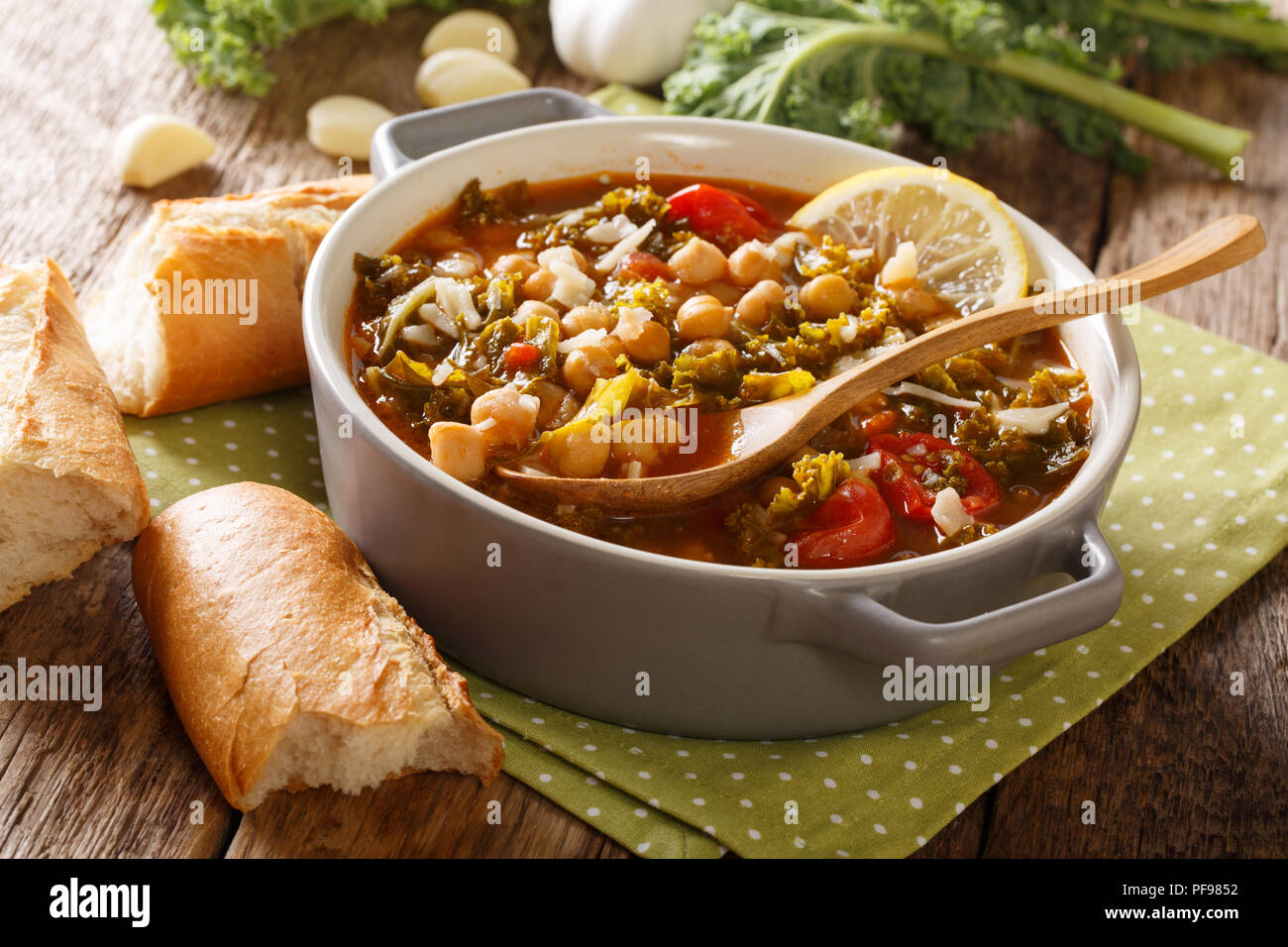 Soup of chickpeas, kale, tomatoes, garlic and potatoes with lemon close up in a bowl on the table. horizontal Stock Photo
