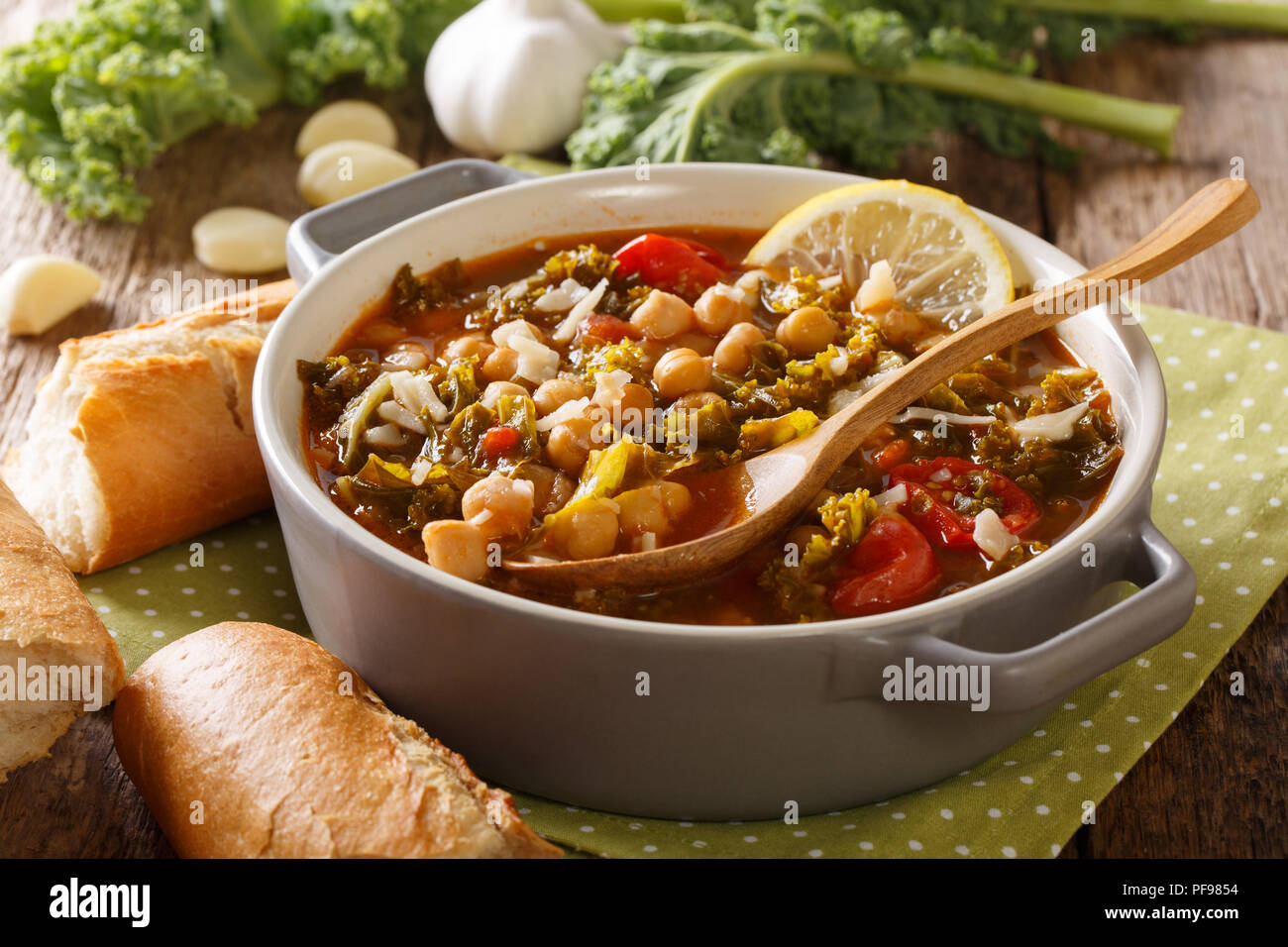 Vegetable stew of chickpeas, kale, tomatoes, garlic and potatoes with lemon close up in a bowl on the table. horizontal Stock Photo