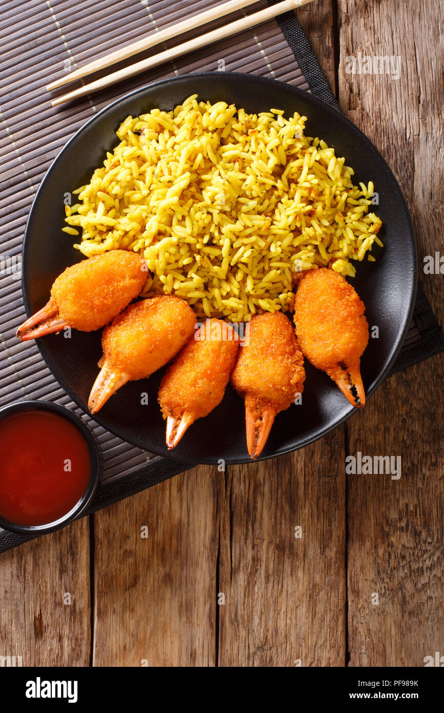Deep fried crab claws in breadcrumbs of surimi with spicy yellow rice close-up on a plate on a table. Vertical top view from above Stock Photo