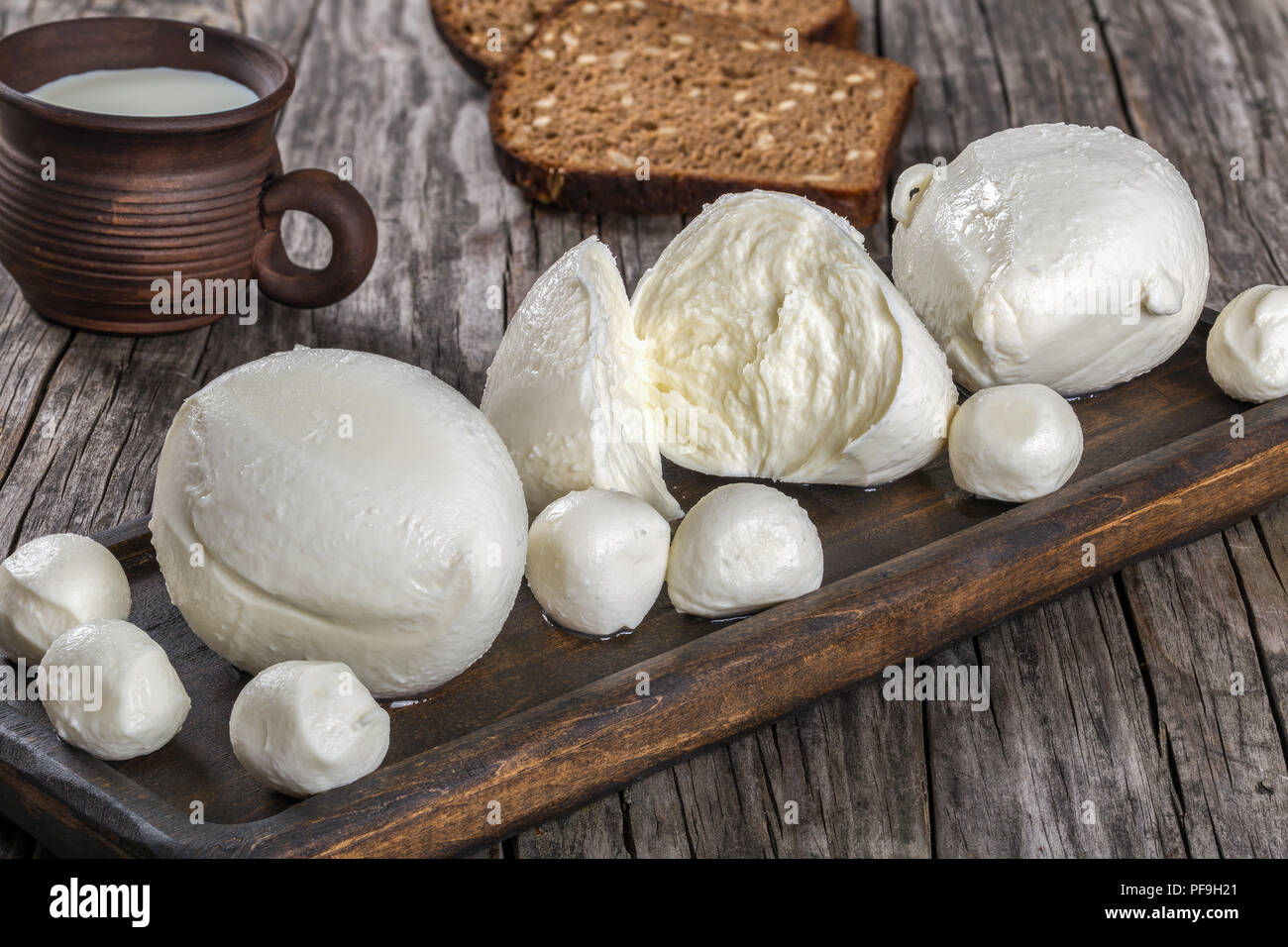 mozzarella balls on a dark board and clay cup with milk on an old rustic table, top view Stock Photo