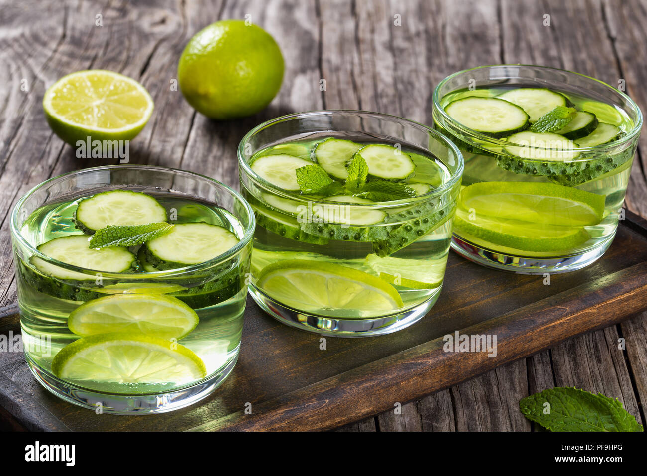 The Most Efficient Drink For Losing Belly Fat - Sassy Water: sliced cucumber, lime and mint in the three glasses on a wooden tray on an old wooden tab Stock Photo