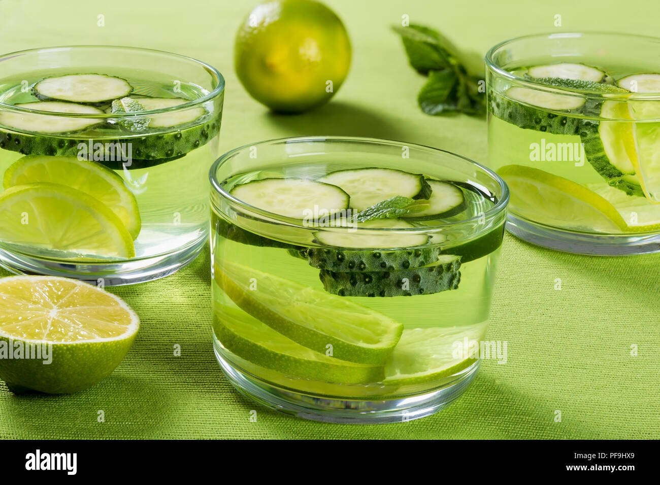 Very Fat Burning Detox Drink - Sassy Water: sliced cucumber, lime and mint in the three glasses on a green  table rib mat, close-up Stock Photo