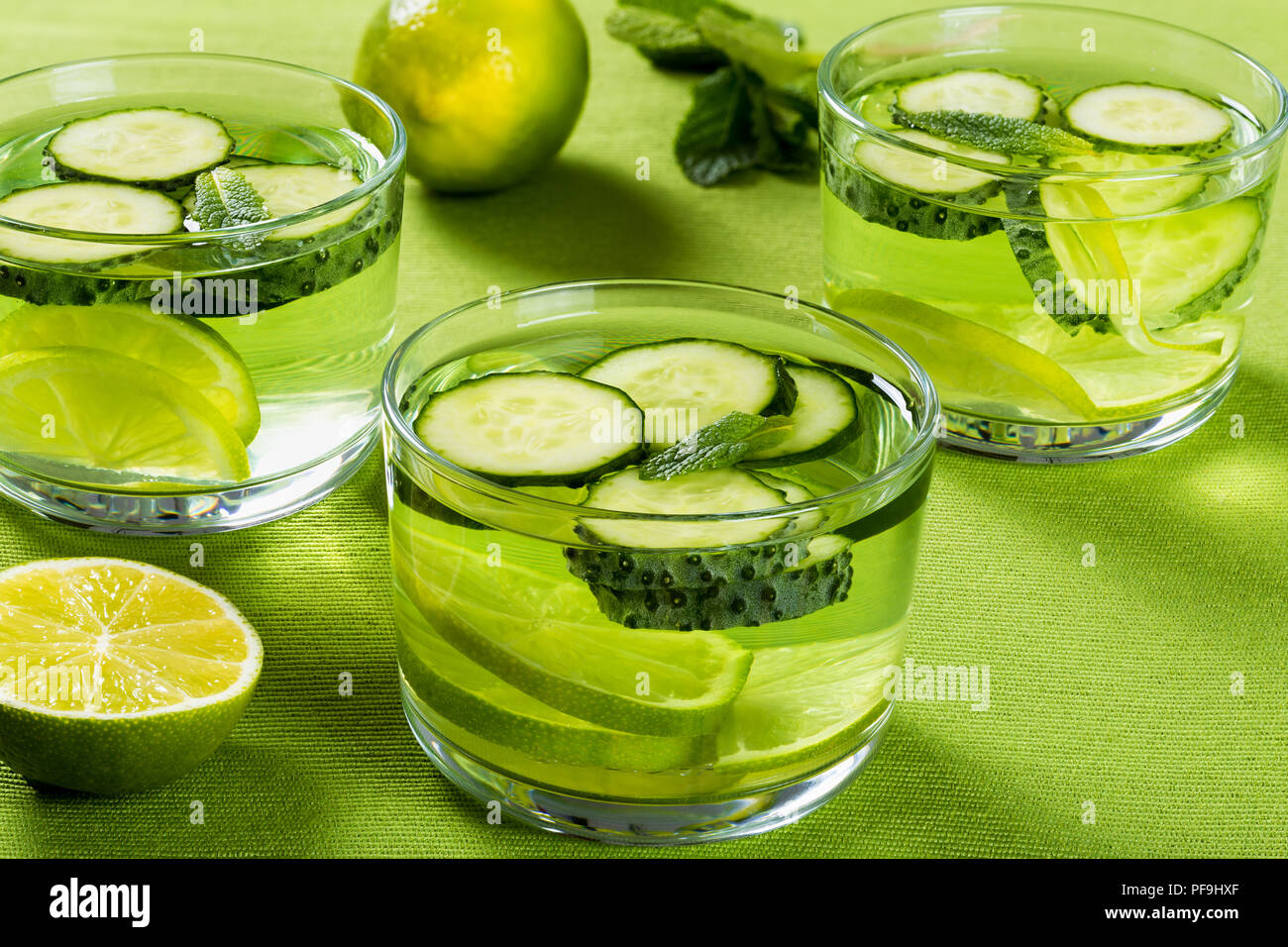 Very Fat Burning Detox Drink - Sassy Water: sliced cucumber, lime and mint in the three glasses on a green  table rib mat, close-up Stock Photo